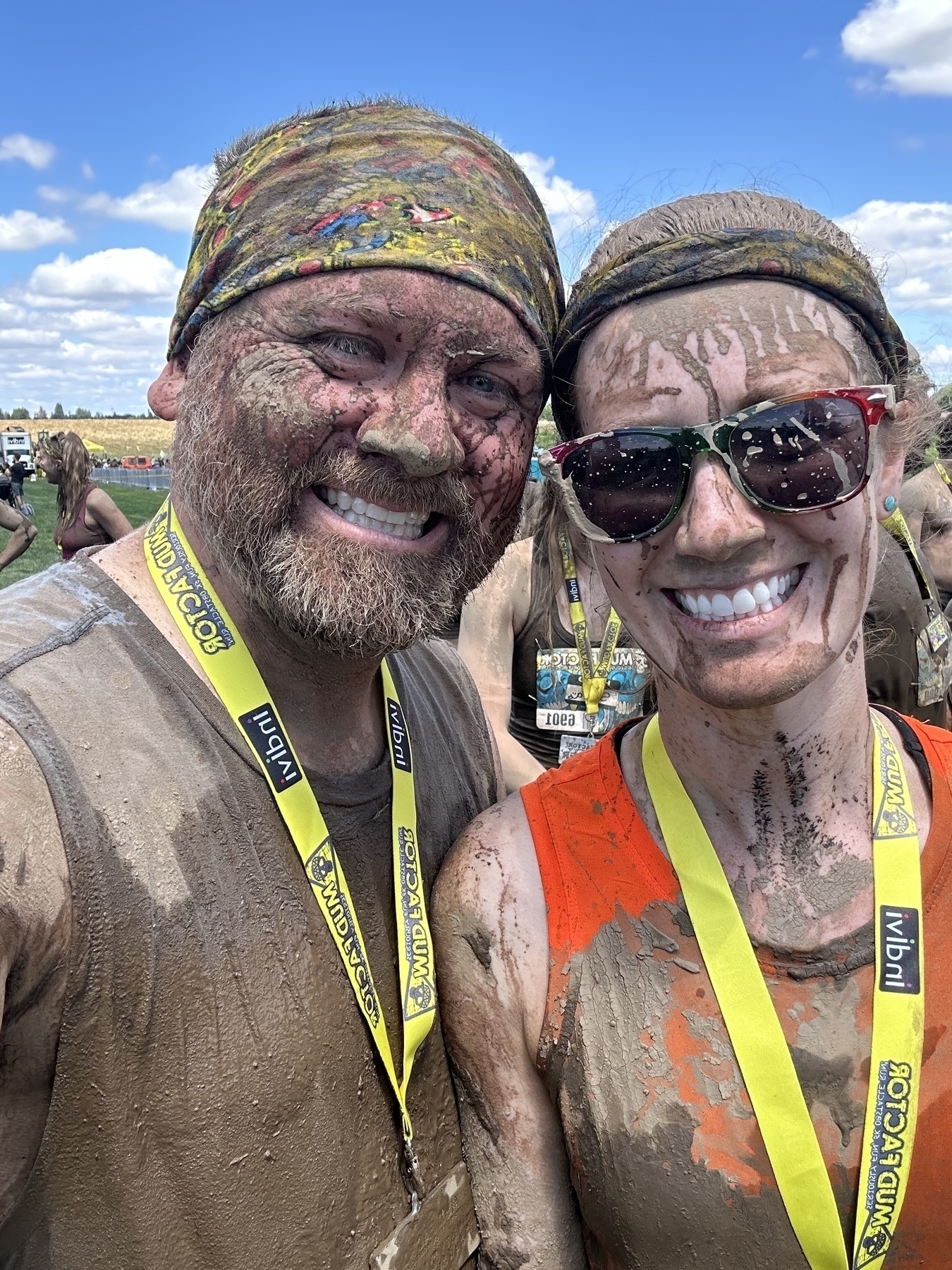 Two people covered in mud are smiling at the camera, wearing headbands and event medals around their necks.