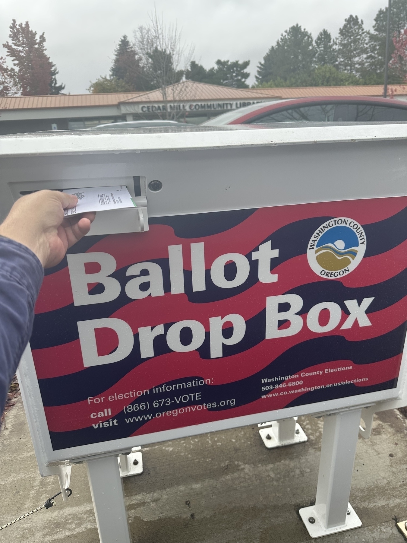 A person is dropping a ballot into a designated ballot drop box located near the Cedar Mill Community Library in Washington County, Oregon.