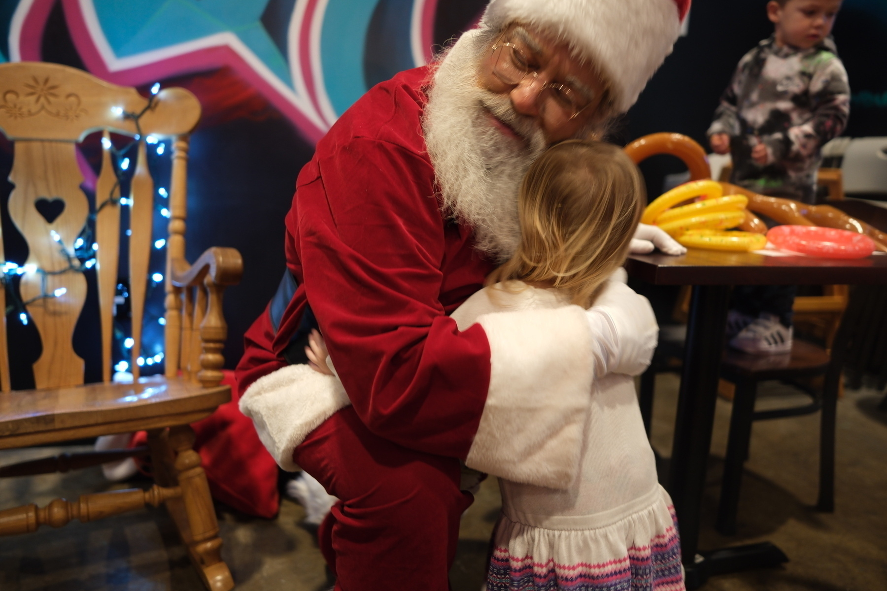 A child is hugging someone dressed as Santa Claus in a festive setting.