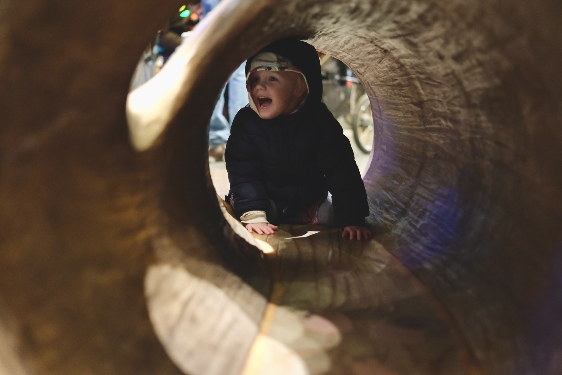 A child is crawling and laughing inside a hollow log.