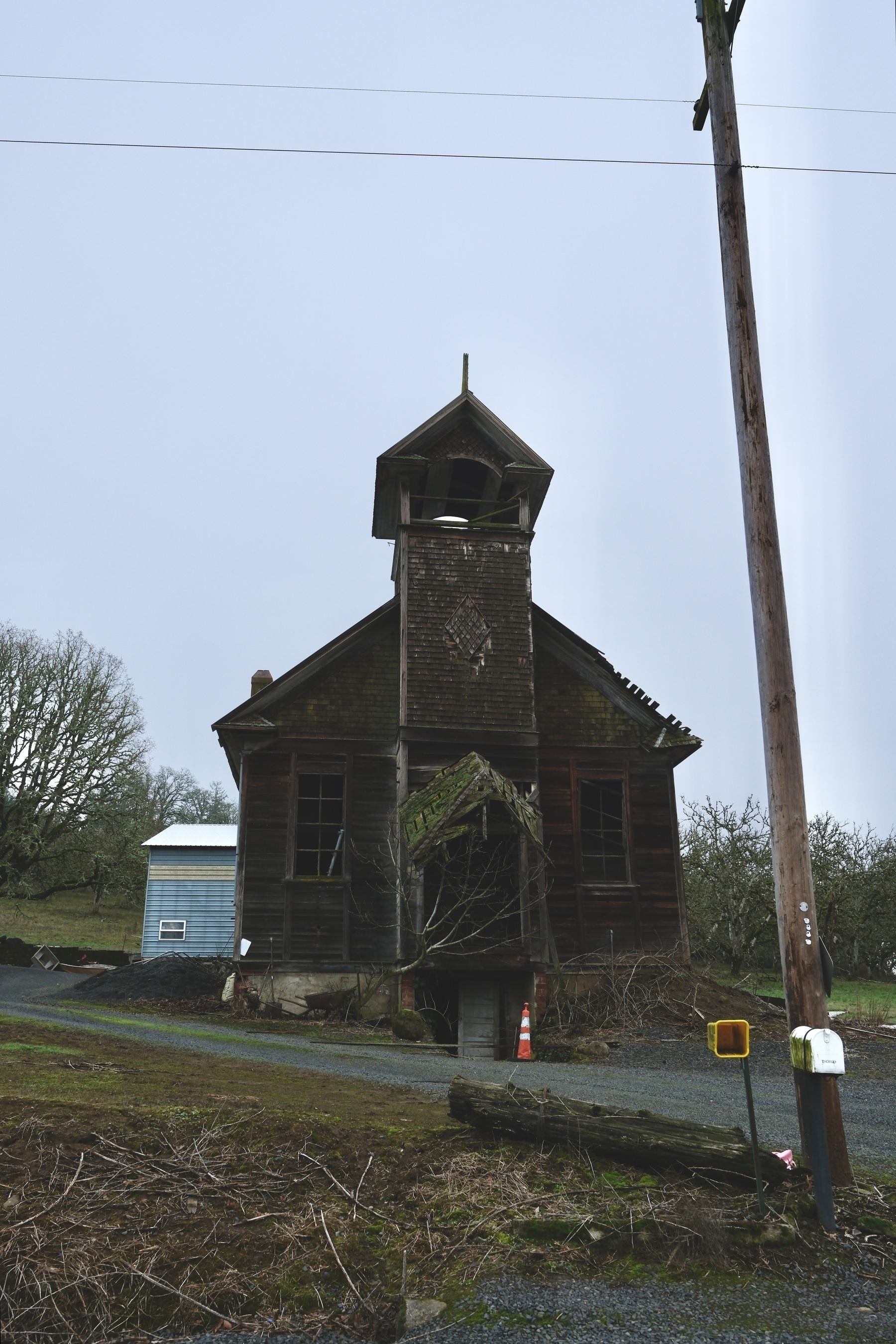 A weathered, abandoned wooden church with a bell tower stands amidst a drab, overcast landscape.