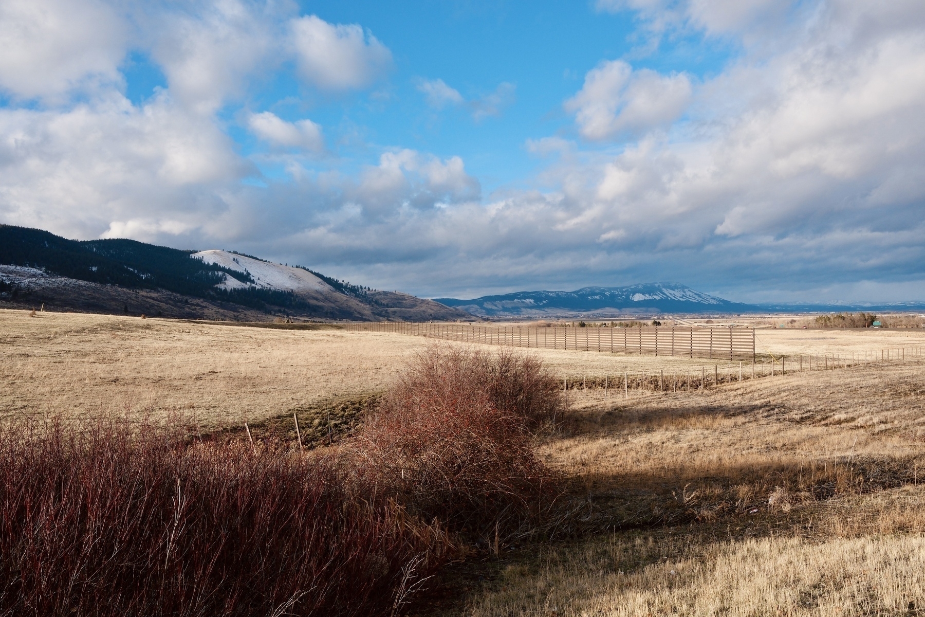 A vast, open landscape features a grassy field, distant mountains, and a partly cloudy sky.