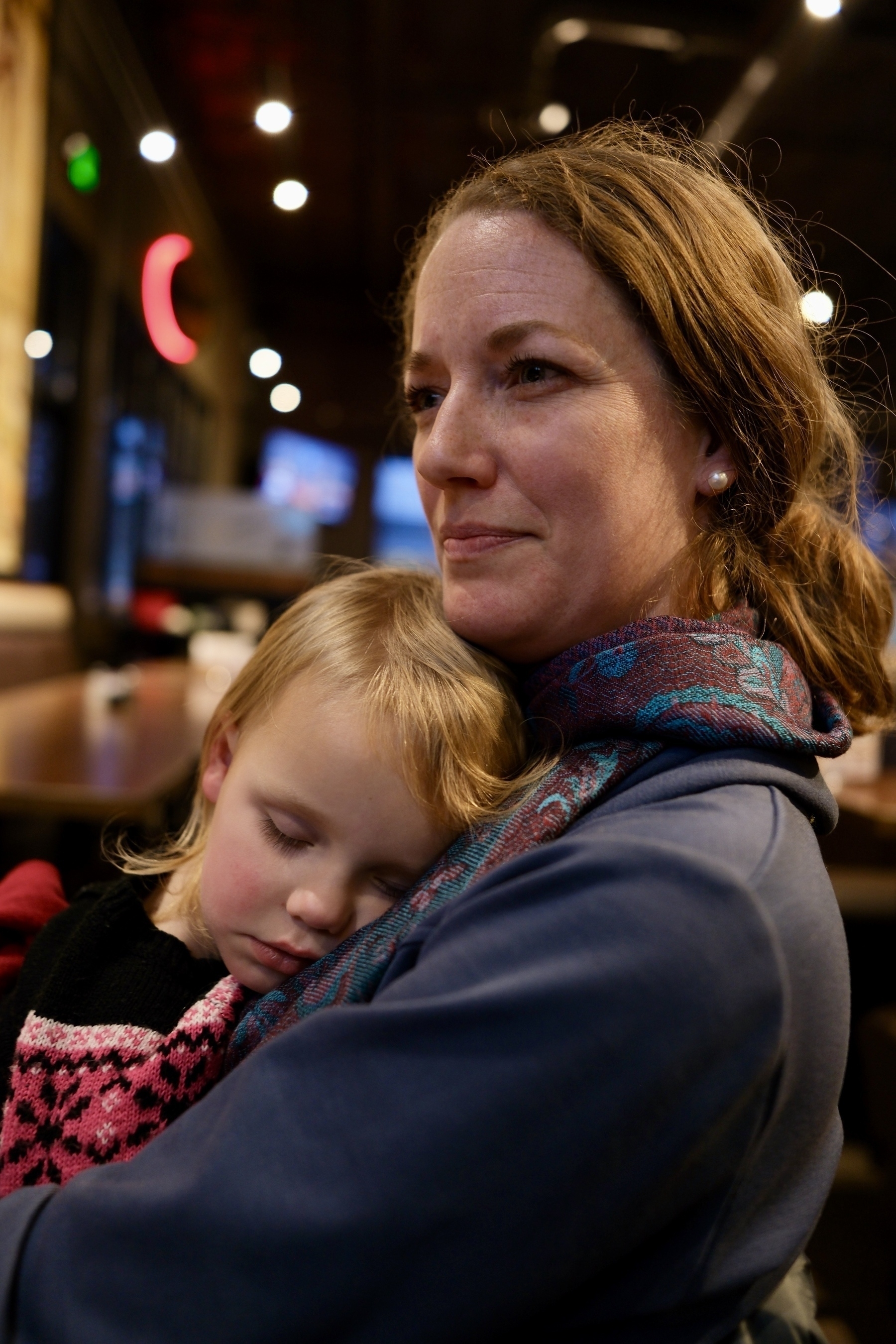 A woman is holding a sleeping child in a cozy setting with soft lighting.